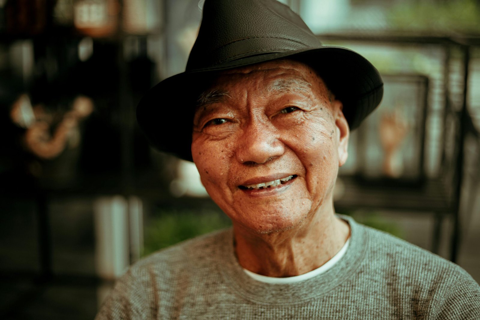 Warm portrait of a smiling elderly man wearing a hat, indoors with soft lighting.
